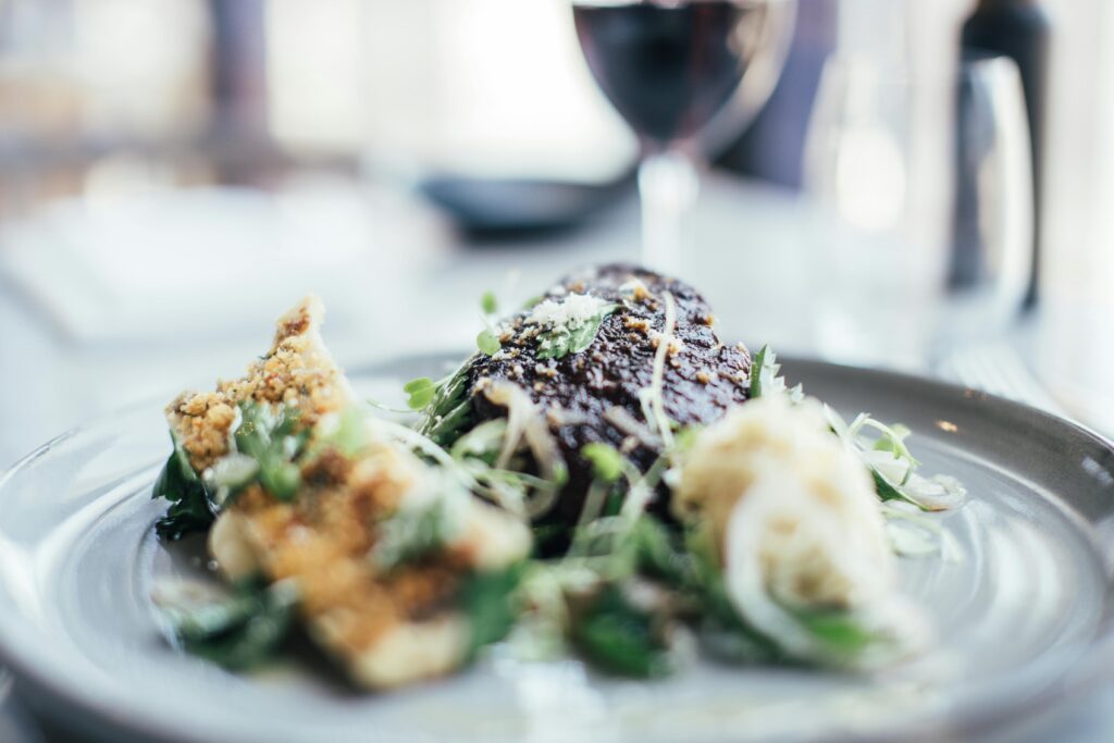 Tasty stuffed celery and grilled steak decorated with fresh green herbs served on plate on table in restaurant with wineglass on blurred background